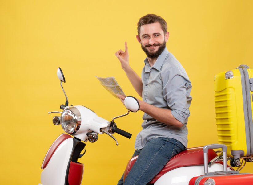 travel-concept-with-smiling-young-man-sitting-motocycle-with-suitcases-it-holding-map-yellow